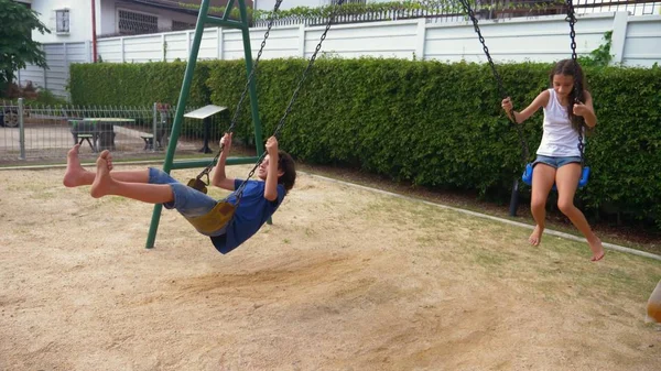 Menino e menina adolescente balançando em um balanço com os pés descalços no gramado verde do quintal de sua casa — Fotografia de Stock