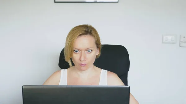 Une femme qui utilise son ordinateur portable, assise à la table, est soudainement surprise et dégoûtée. Des émotions humaines. Dépendance à Internet . — Photo