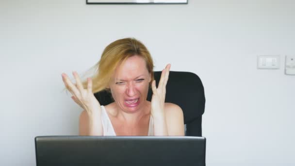 En kvinna med hennes laptop, sitter vid bordet, är plötsligt skrämd och äcklad. Mänskliga känslor. Internetberoende. — Stockvideo