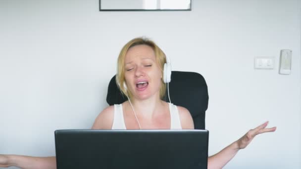 Женщина, использующая ноутбук, сидит за столом и смеется и разговаривает. Человеческие эмоции. Интернет-зависимость . — стоковое видео