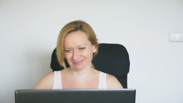 Una mujer que usa su portátil está sentada a la mesa, riendo y hablando. Emociones humanas. Adicción a Internet . — Vídeo de stock