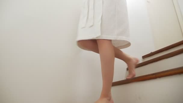 Närbild. kvinnliga ben stiger till toppen av en trä stege. kvinna i en morgonrock går upp för trappan — Stockvideo