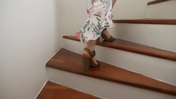 Primo piano. le gambe della donna in sandali scendono le scale di legno. una donna con una bella gonna lunga cammina per le scale . — Video Stock
