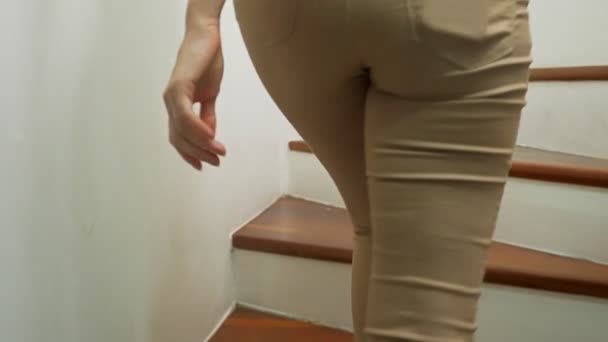 Primo piano, gambe femminili in pantaloni aderenti beige e sandali con tacco a spillo che camminano lungo una scala moderna in legno — Video Stock