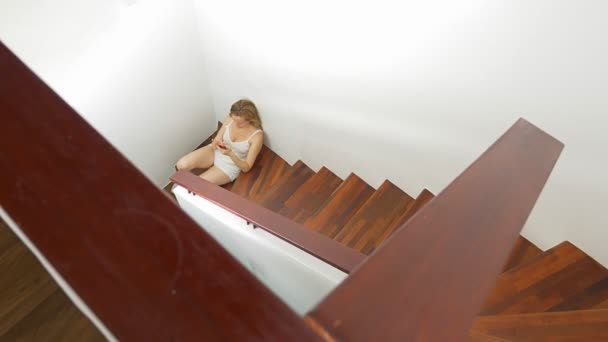 穿着短裤的女孩坐在家里的楼梯上, 用智能手机 — 图库视频影像