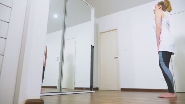 Mujer estirándose cerca del espejo en su apartamento. El concepto de un estilo de vida saludable, no un deporte profesional . — Vídeo de stock