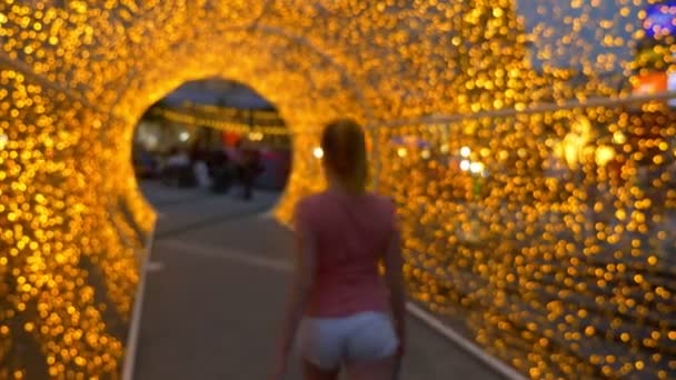 Schönes Mädchen in weißen Shorts geht durch ein Gewölbe aus goldenen Lichtern. — Stockvideo