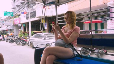Tayland, Pattaya, Jomtien Beach, 07. 12. 2018. Güzel bir genç kadın bir tuk-tuk öğleden sonra sürmek ve bir akıllı telefon kullanır. Turizm kavramı