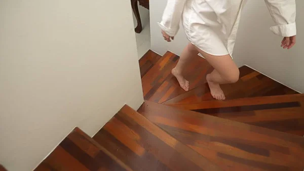 Gros plan. Les pieds des femmes montent les escaliers en bois. une femme en chemise homme monte à l'étage — Photo