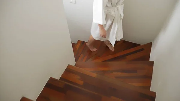 Primer plano. piernas femeninas se eleva a la parte superior de una escalera de madera. mujer en una bata sube los escalones — Foto de Stock