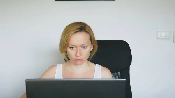 Une femme utilisant son ordinateur portable, assise à la table, en colère et irritée, jure. Des émotions humaines. concept de dépendance à Internet . — Photo