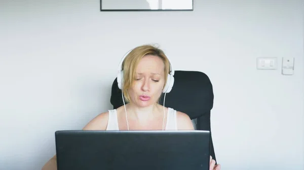 Eine Frau sitzt mit ihrem Laptop am Tisch, lacht und redet. Menschliche Emotionen. Internetsucht. — Stockfoto