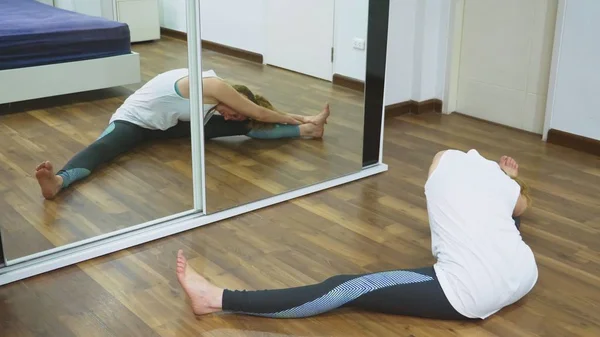 Жінка розтягується біля дзеркала у своїй квартирі. Концепція здорового способу життя, а не професійного спорту . — стокове фото