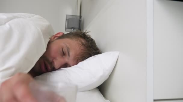 Zieke jongeman met koorts in slaap in bed, gedekt door een deken — Stockvideo