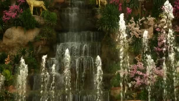 ピンクの花と緑の葉に囲まれた大きな人工滝 — ストック動画