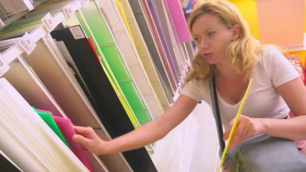 Papeles de arte coloridos en un estante para la venta en una tienda de papelería. mujer elige hojas de papel de color en la tienda . — Vídeo de stock