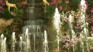 büyük bir yapay şelale çerçeveli pembe çiçekler ve yeşil yaprakları.