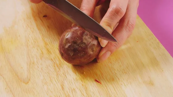 Visão superior, a mão feminina corta o fruto com uma faca em uma tábua de madeira, maracuya. O conceito de comida saudável natural . — Fotografia de Stock