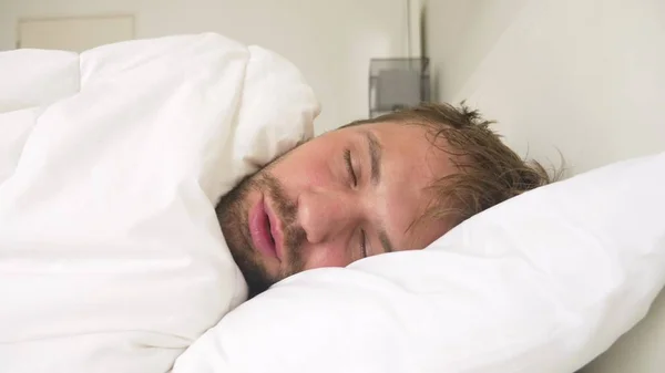 sick young man with fever asleep in bed, covered by a blanket