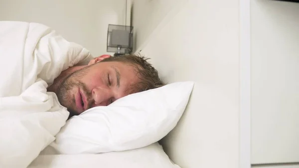 sick young man with fever asleep in bed, covered by a blanket