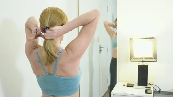 The concept of excess weight and weight loss. Woman in sportswear looking at herself in the mirror in the bedroom — Stock Photo, Image