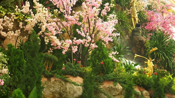Una gran cascada artificial enmarcada por flores rosadas y hojas verdes . — Foto de Stock