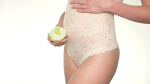 Primer plano de una mujer embarazada sosteniendo una flor de loto blanca junto a su vientre — Foto de Stock