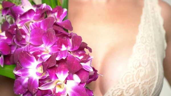 Primer plano. primer plano del pecho femenino con un ramo grande de orquídeas en sus manos. concepto de salud mamaria femenina — Foto de Stock