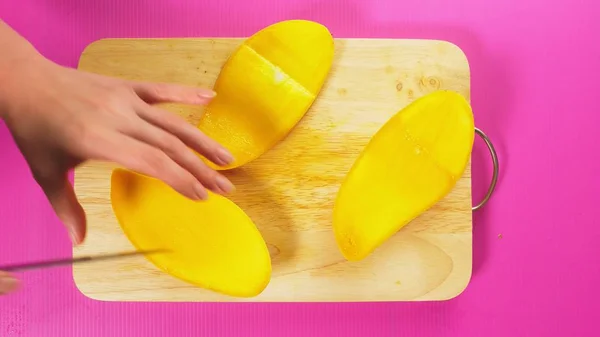 Vista superior, a mão feminina corta frutas com uma faca em uma tábua de madeira, manga. O conceito de comida saudável natural . — Fotografia de Stock