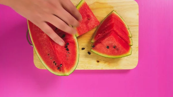 Vista superior, a mão feminina corta frutas com uma faca em uma tábua de madeira, melancia vermelha. O conceito de comida saudável natural . — Fotografia de Stock