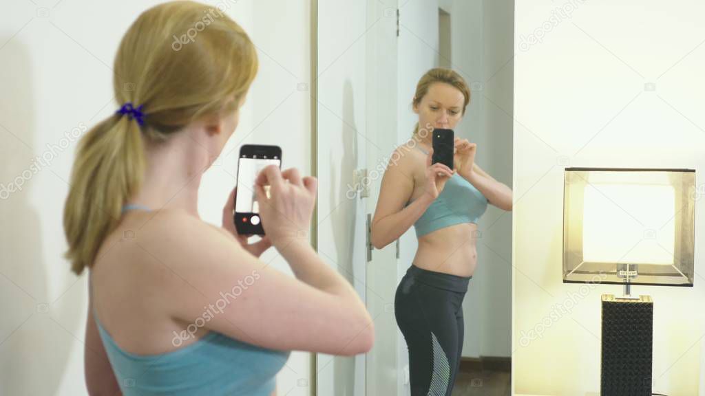 The concept of overweight and weight loss. A woman looks at herself in the mirror and photographs her figure. to compare the results before and after losing weight.