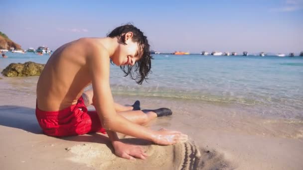 Мальчик-подросток строит замок из песка на тропическом пляже — стоковое видео