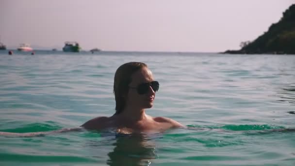 Szőke lány a fürdőruhát és fekete napszemüveg. Szexi test gyönyörű modell úszik a víz kék tenger