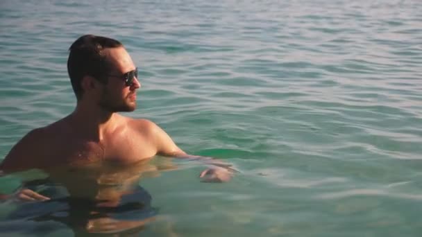 Portrait of a handsome young man with a beard in sunglasses relaxed in crystal clear sea water — Stock Video