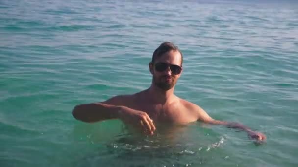 Портрет красивого молодого человека с бородой в солнечных очках, расслабленного в кристально чистой морской воде — стоковое видео