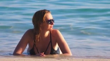 Sarışın kız siyah mayo ve bir beyaz kum Plajı üzerinde siyah güneş gözlüğü. Deniz kenarında güzel model seksi vücut ile sunbathes