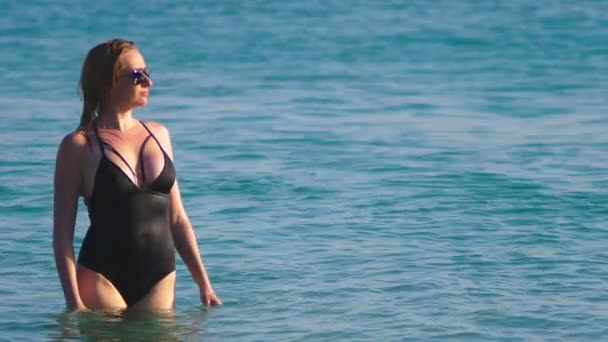 La fille la blonde en maillot de bain noir et des lunettes noires. Beau modèle avec corps sexy s'amuse dans de l'eau de mer cristalline . — Video