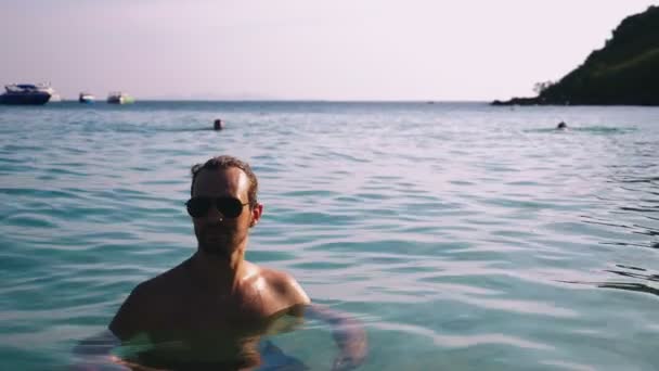 Portret van een knappe jonge man met een baard in zonnebril ontspannen in kristalhelder zeewater — Stockvideo