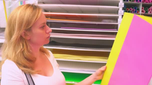 Sztuki kolorowe papiery na półce na sprzedaż w sklepach z artykułami papierniczymi. Kobieta wybiera arkusze kolorowego papieru w sklepie. — Wideo stockowe