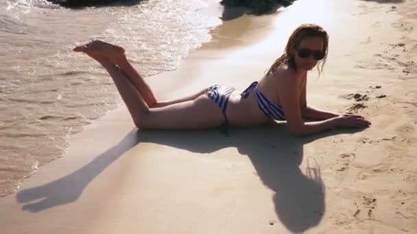 Блондинка в купальнику і чорні сонцезахисні окуляри на білому піщаному пляжі біля океану у відпустці. Красива модель з сексуальним плаванням тіла у блакитній морській воді — стокове відео