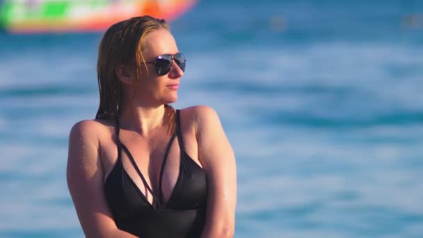 La fille la blonde en maillot de bain noir et des lunettes noires. Beau modèle avec corps sexy s'amuse dans de l'eau de mer cristalline . — Video