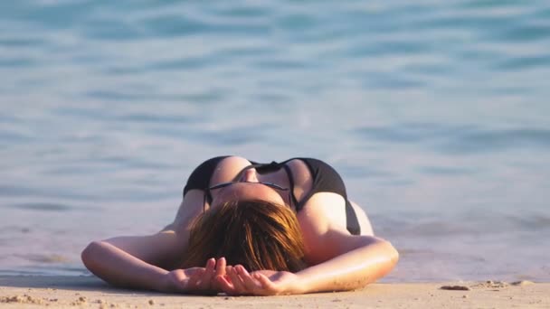Sarışın kız siyah mayo ve bir beyaz kum Plajı üzerinde siyah güneş gözlüğü. Deniz kenarında güzel model seksi vücut ile sunbathes — Stok video