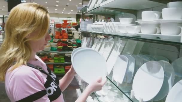 Een vrouw gerechten in de winkel koopt, onderzoekt verschillende items van gerechten. — Stockvideo