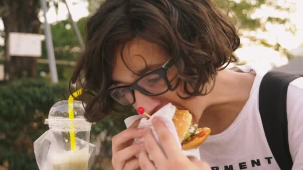 Teenie-Junge isst Hamburger und Pommes im Outdoor-Café. Nahaufnahme — Stockvideo