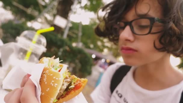 야외 카페에서 햄버거와 감자 튀김을 먹는 십 대 소년. 클로즈업 — 비디오