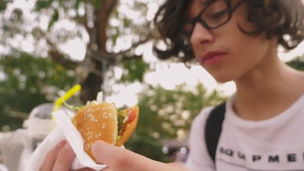 Хлопчик їсть гамбургер та картоплю фрі у відкритому кафе. крупним планом — стокове відео