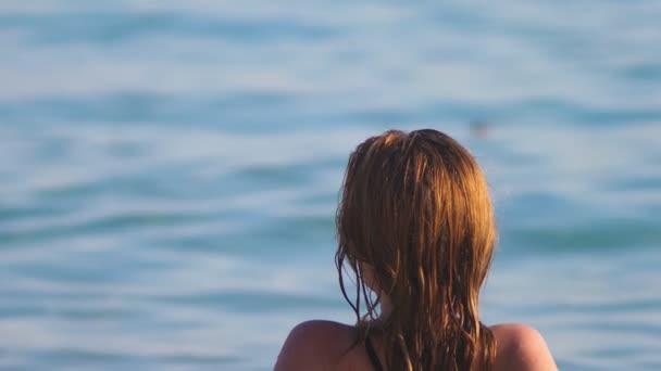 Ξανθιά κοπέλα στο μαύρο μαγιό και μαύρα γυαλιά για μια παραλία με λευκή άμμο. Το όμορφο μοντέλο με το προκλητικό σώμα sunbathes δίπλα στη θάλασσα — Αρχείο Βίντεο