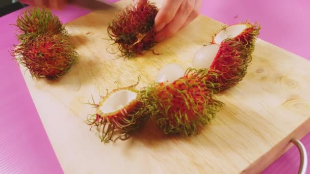 Female hands clean rambutan on a wooden board. The concept of natural healthy food. — Stock Video