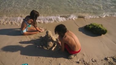 Gençler, kız ve erkek kardeşim tropikal bir plajda kumdan kale yapma