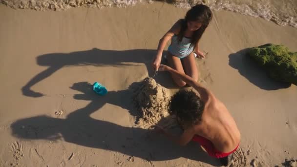 Adolescentes, irmão e irmã fazendo um castelo de areia em uma praia tropical — Vídeo de Stock